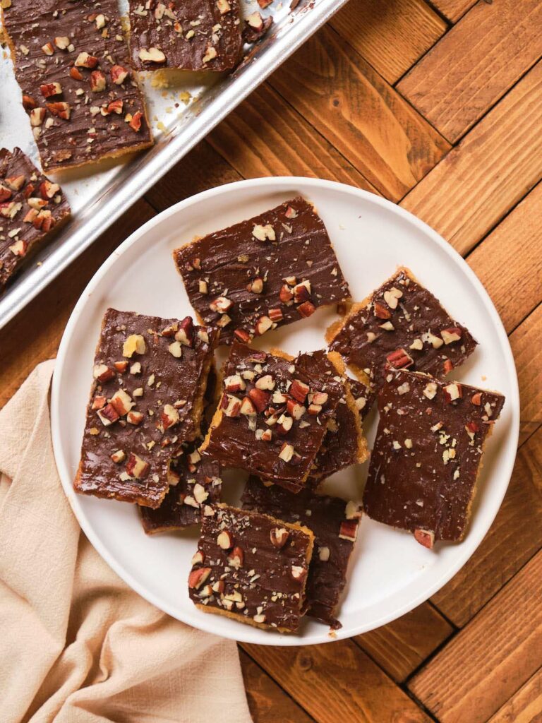 A plate of saltine toffee bars topped with chopped nuts on a wooden table.