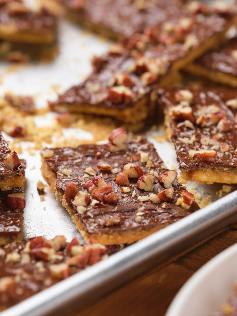 Saltine toffees topped with chopped pecans on a baking sheet.