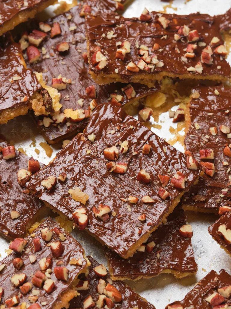 Saltine toffee squares topped with chopped nuts, arranged in a pile.