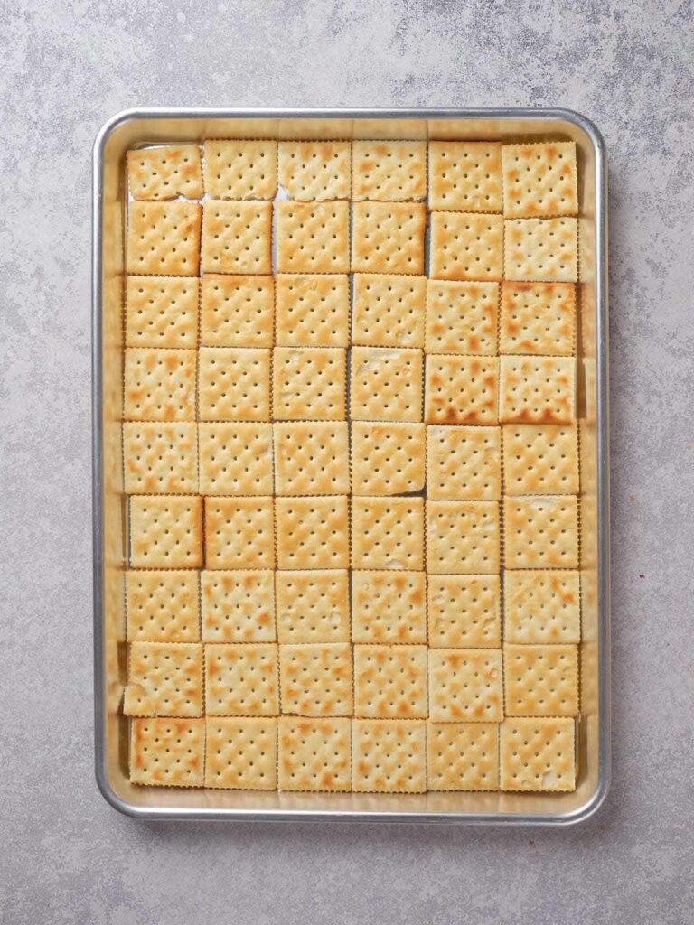 A baking sheet filled with evenly arranged square crackers.