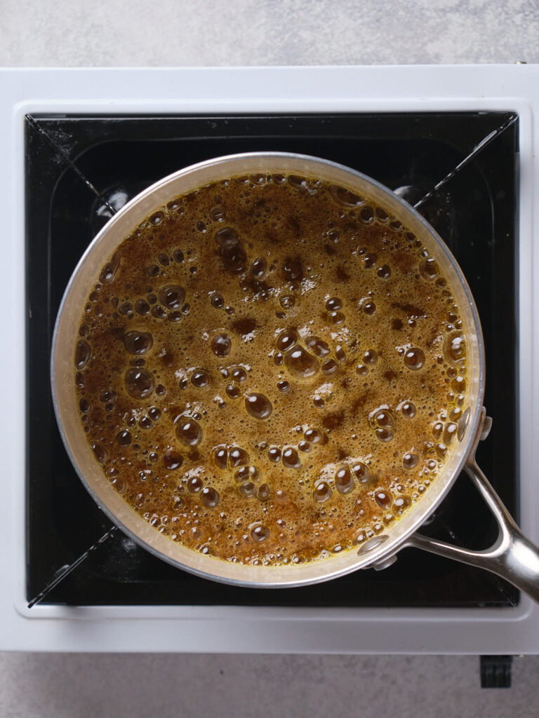 A pot of boiling caramel sauce on a stove with bubbles forming on the surface.