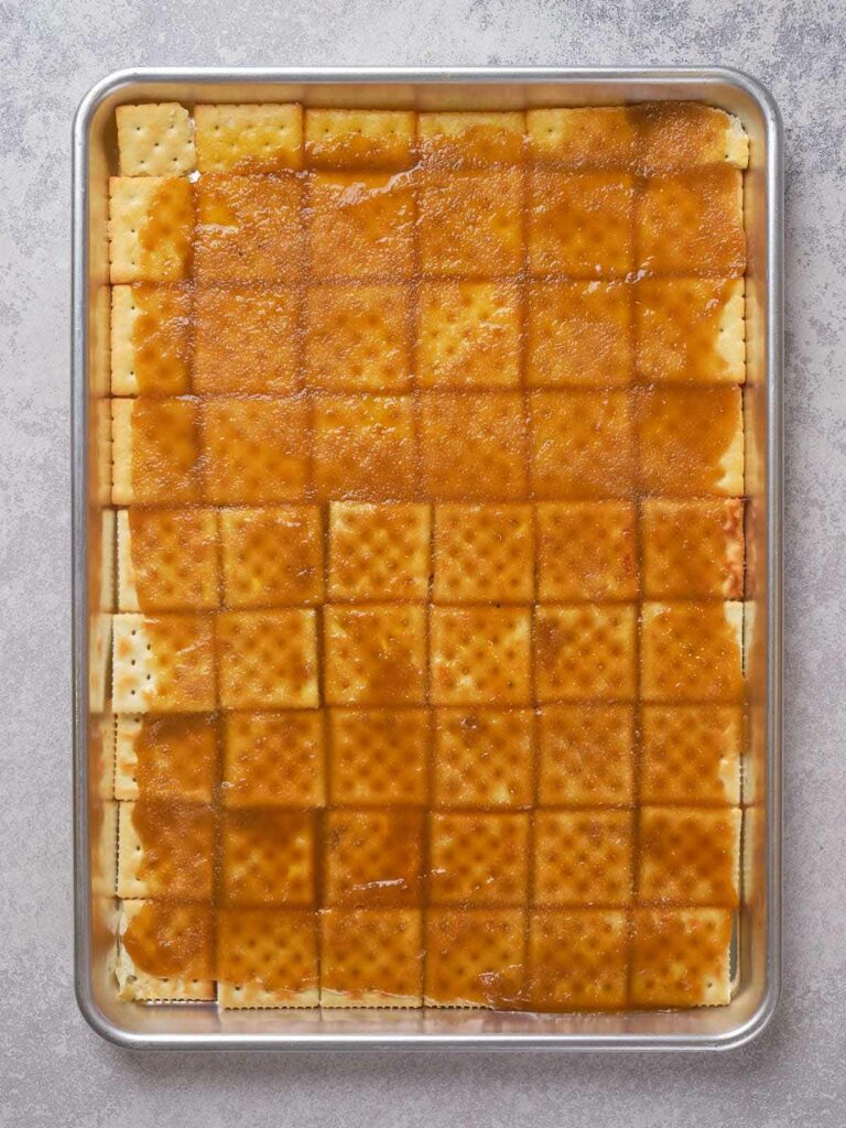 Baking tray with a grid of crackers topped with a caramel-like sauce.