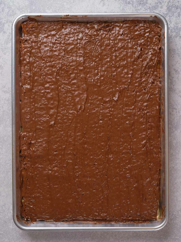 A rectangular sheet pan filled with a thick layer of chocolate frosting on top of a dessert.