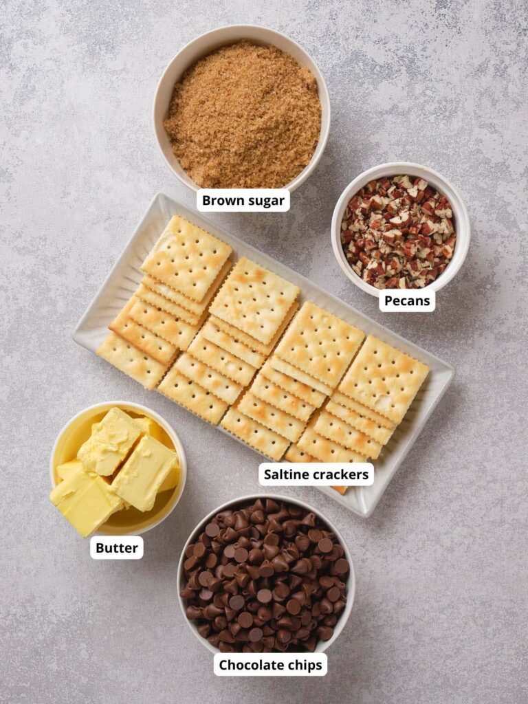 Ingredients on a table: brown sugar, pecans, saltine crackers, butter, and chocolate chips in bowls.