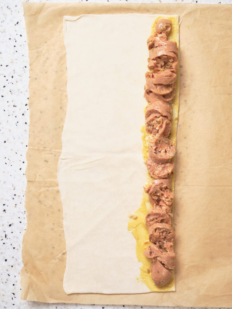 Unrolled pastry on parchment paper with sausage filling lined along one edge, ready for wrapping.