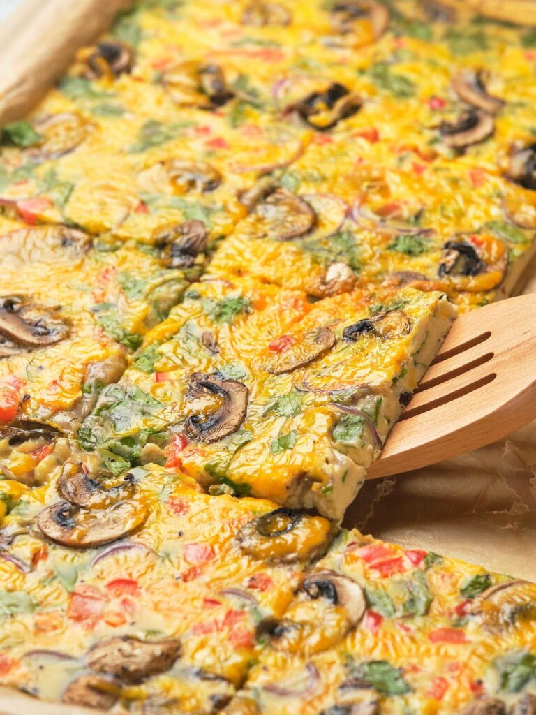 Sheet pan eggs with a wooden spatula lifting one piece.