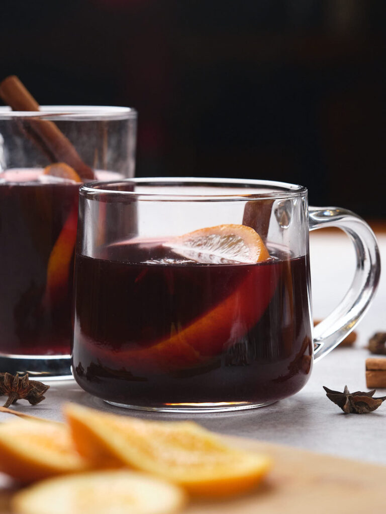 Two glass mugs of mulled wine with orange slices and cinnamon sticks.