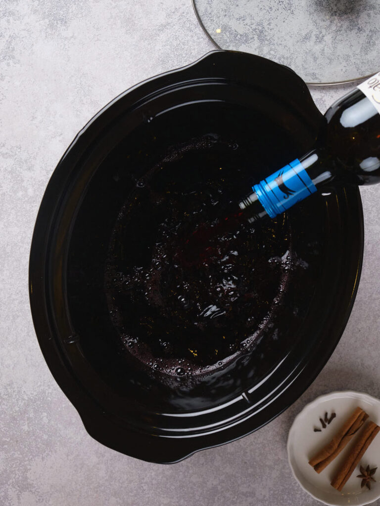 A person pours red wine into a slow cooker.