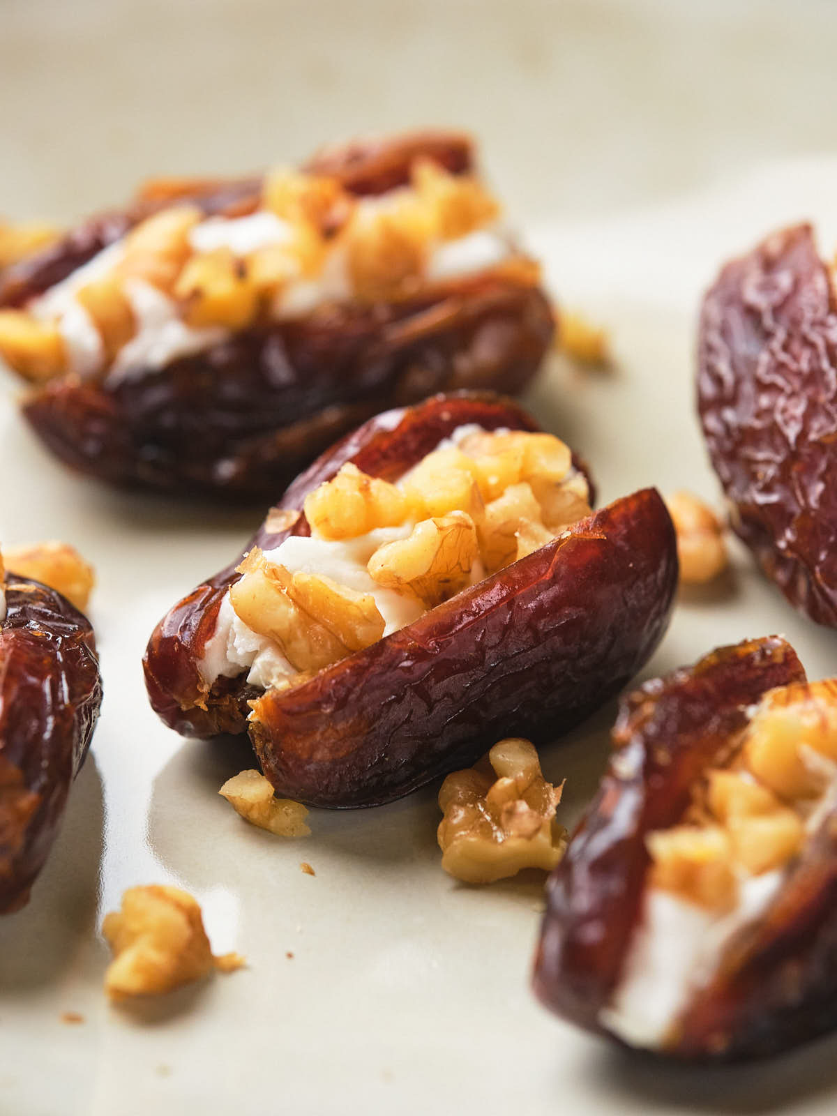 Close-up of dates stuffed with a creamy filling and topped with chopped nuts on a light-colored surface.