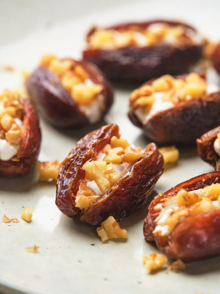 Close-up of dates stuffed with chopped nuts, arranged on a light-colored plate.