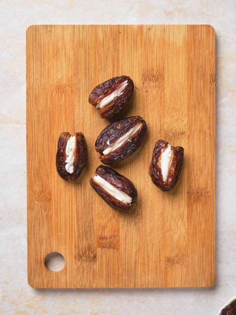 Stuffed dates on a wooden board on a white surface.