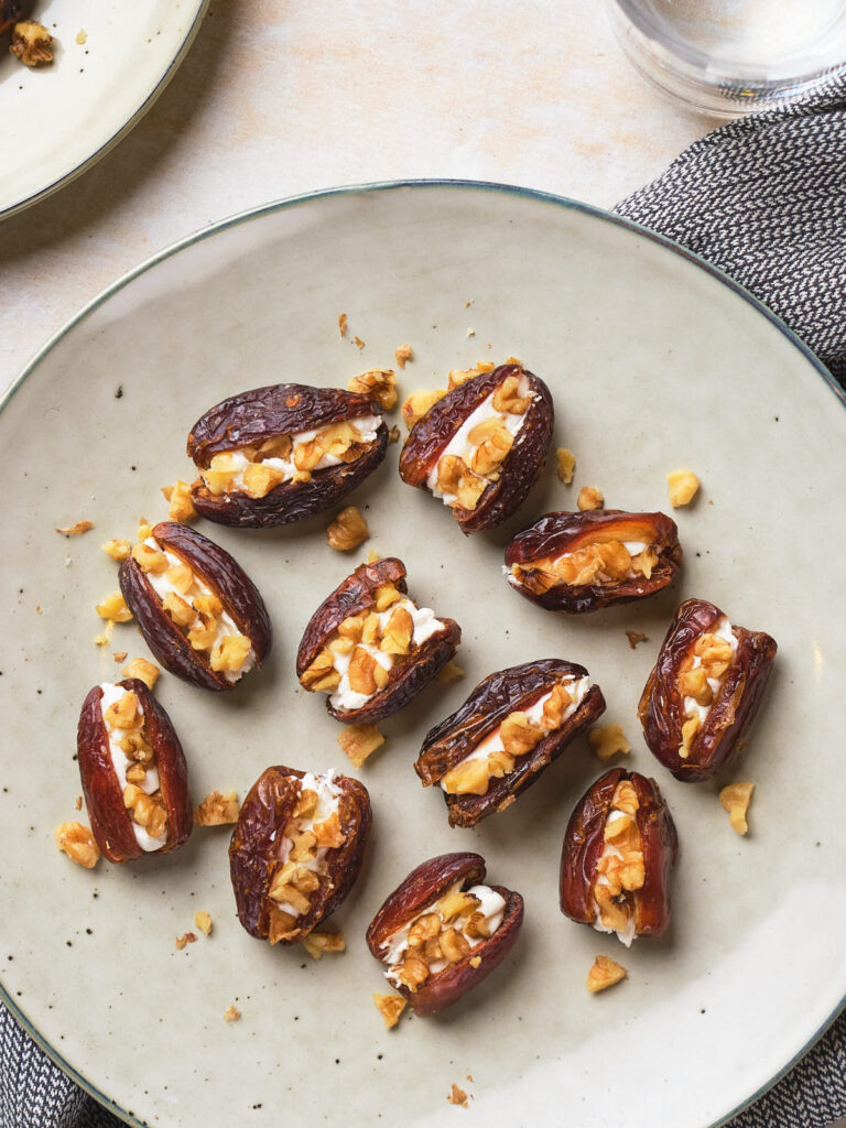 Plate of dates stuffed with cream and chopped nuts, arranged neatly.