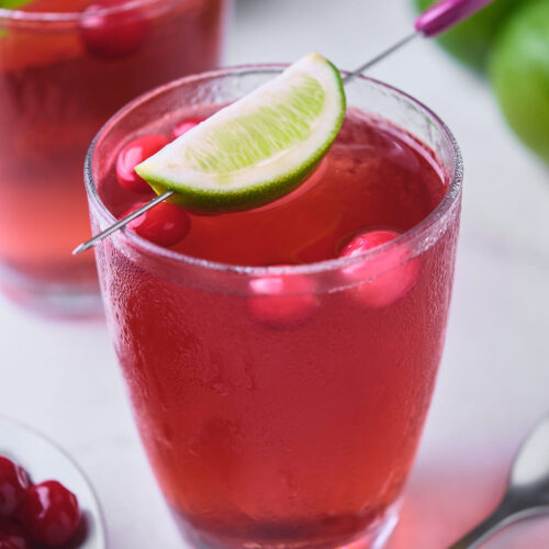 A glass filled with vodka cranberry, garnished with a lime wedge and red berries.