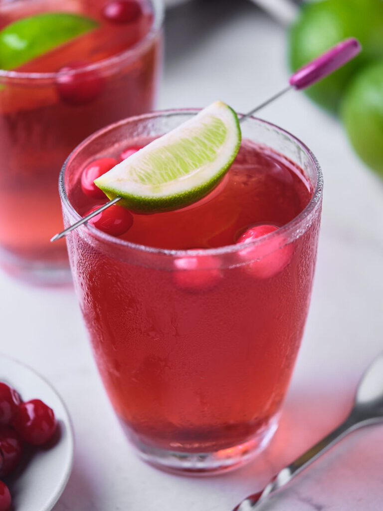 A glass filled with vodka cranberry, garnished with a lime wedge and red berries.