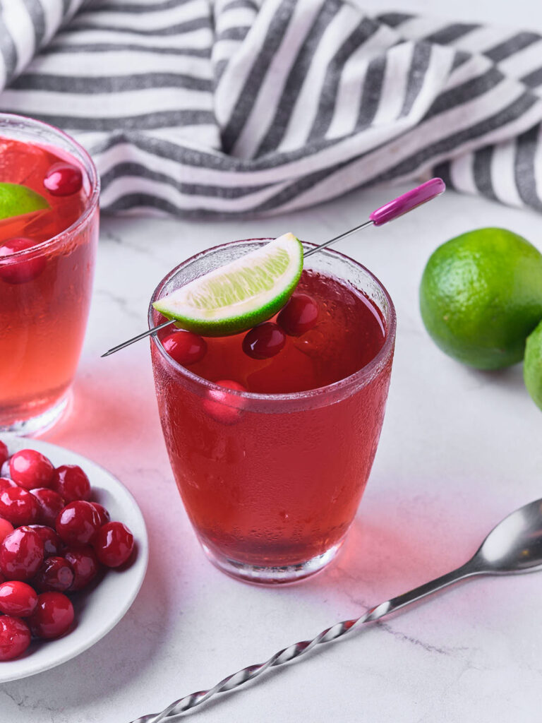 Two glasses of vodka cranberry garnished with cranberries and lime.