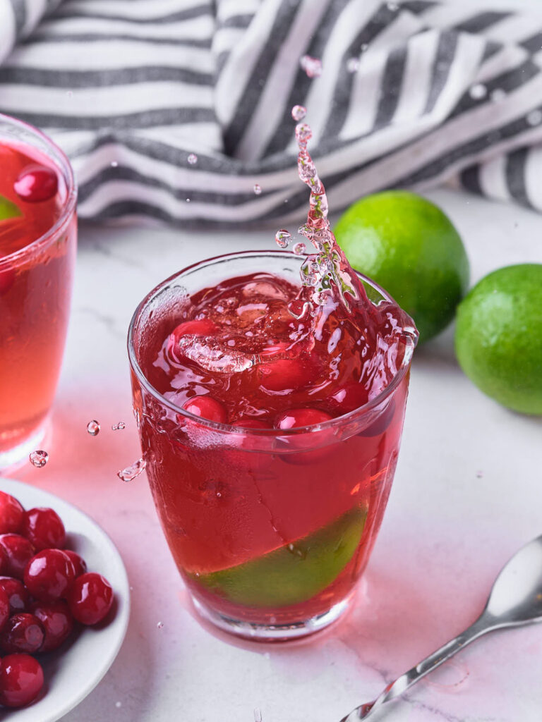 A glass of vodka cranberry with ice cubes and lime slices.