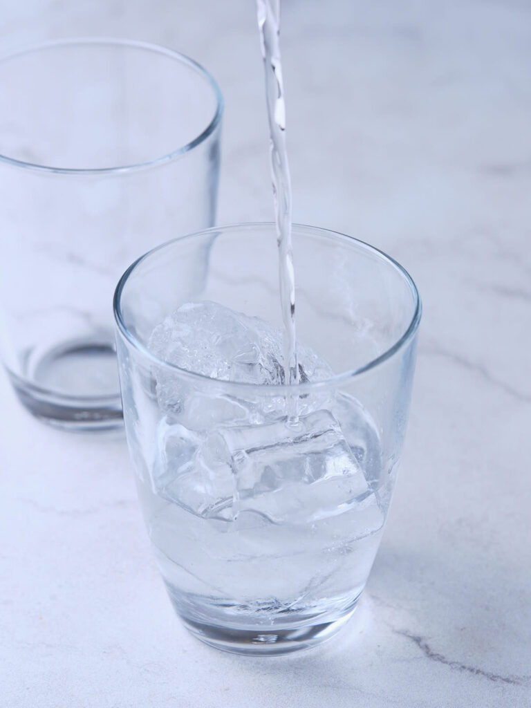 A clear liquid is being poured into a glass filled with ice cubes.