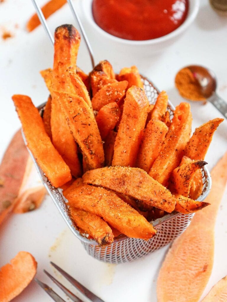 A basket of seasoned sweet potato fries with a dish of ketchup in the background.