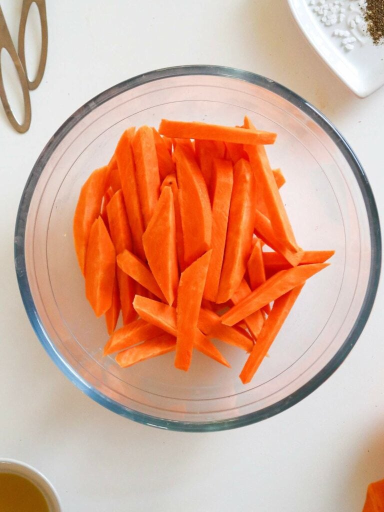 A glass bowl filled with sliced sweet potatoes on a white surface.