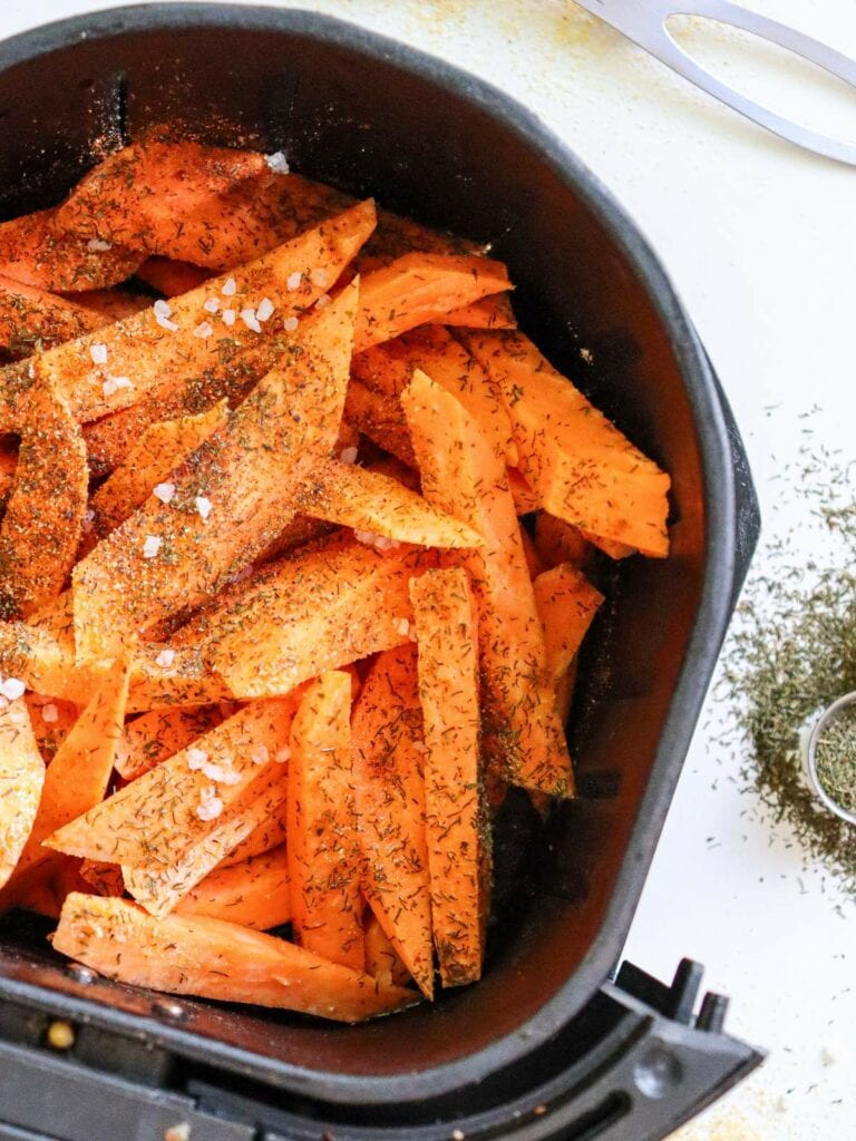 Sweet potato fries seasoned with herbs and salt in an air fryer basket, ready for cooking.