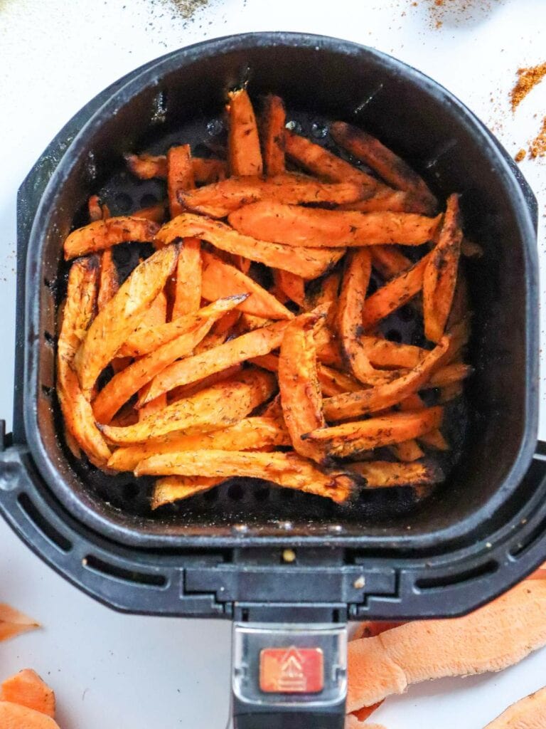 Sweet potato fries in an air fryer basket, seasoned and cooked.