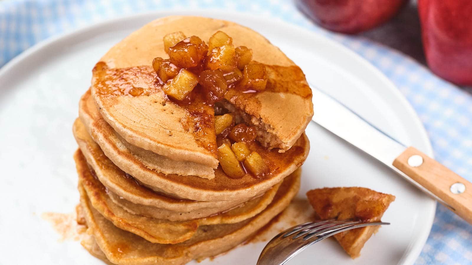 A stack of applesauce pancakes topped with caramelized apple pieces on a white plate.