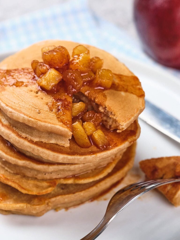 Stack of pancakes topped with caramelized apple cubes and syrup, with a fork holding a cut piece.