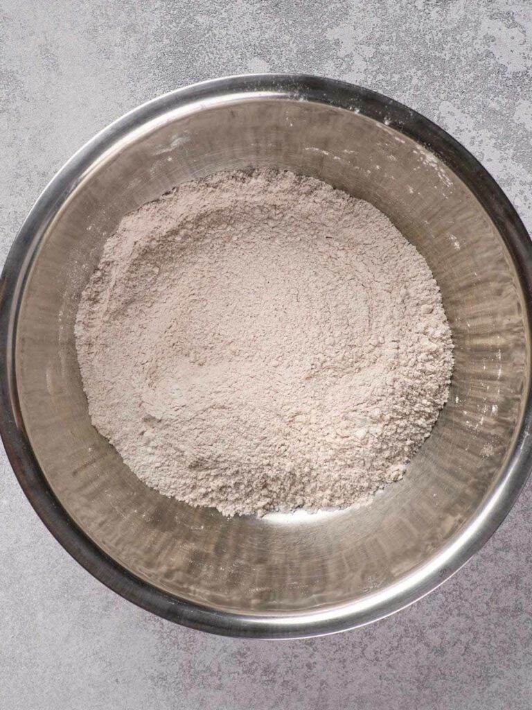 A metal bowl filled with flour placed on a gray surface.