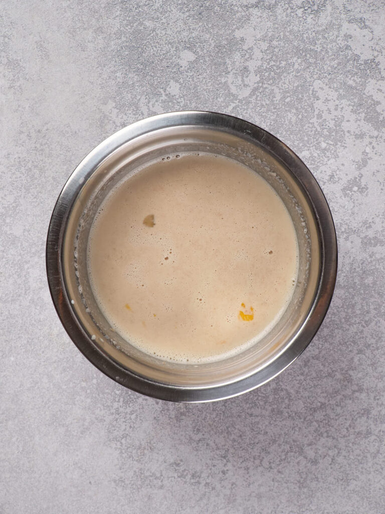 A stainless steel bowl containing a light beige liquid with a few small floating particles.