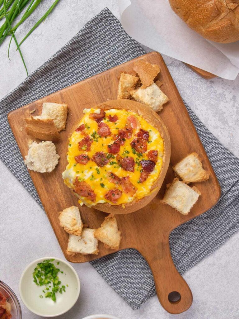 Cheese and bacon cob loaf surrounded by cubed bread pieces on a wooden board.