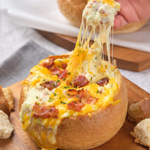 A bread bowl filled with melted cheese, bacon, and herbs.