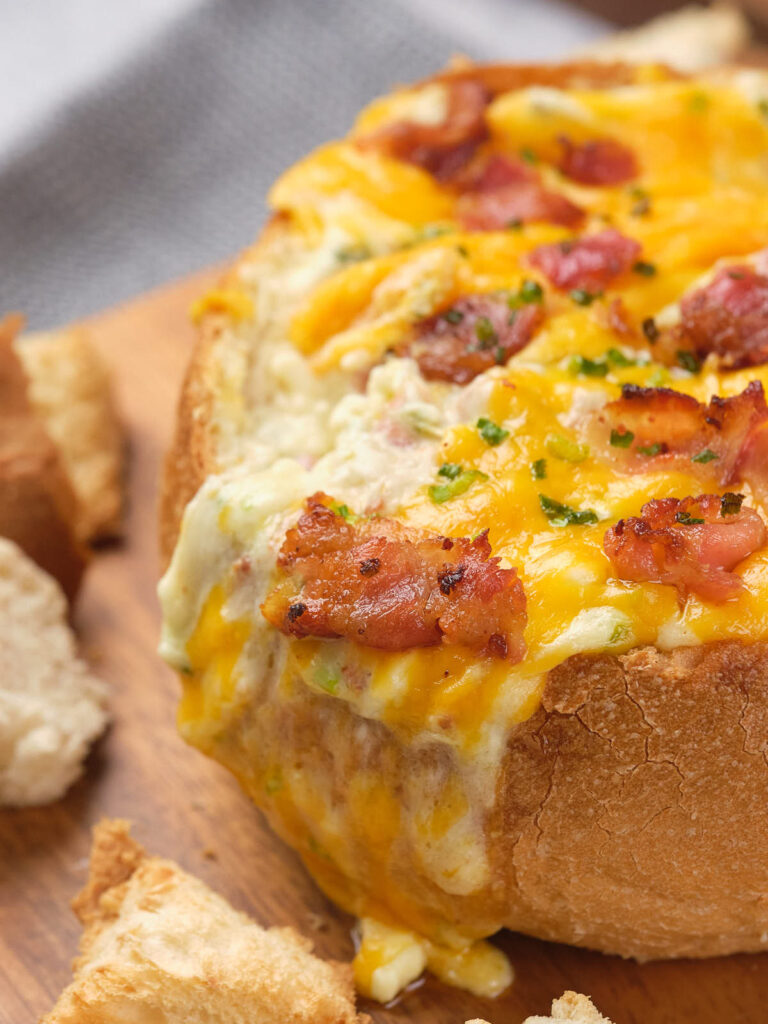 A bread bowl filled with creamy cheese dip topped with bacon and herbs.