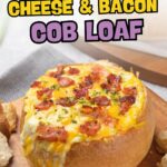 Cheese and bacon-filled cob loaf surrounded by bread pieces on a wooden board.