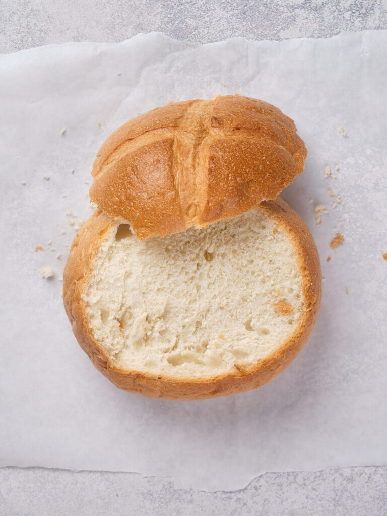 A round loaf of bread with the top cut off, placed on parchment paper.