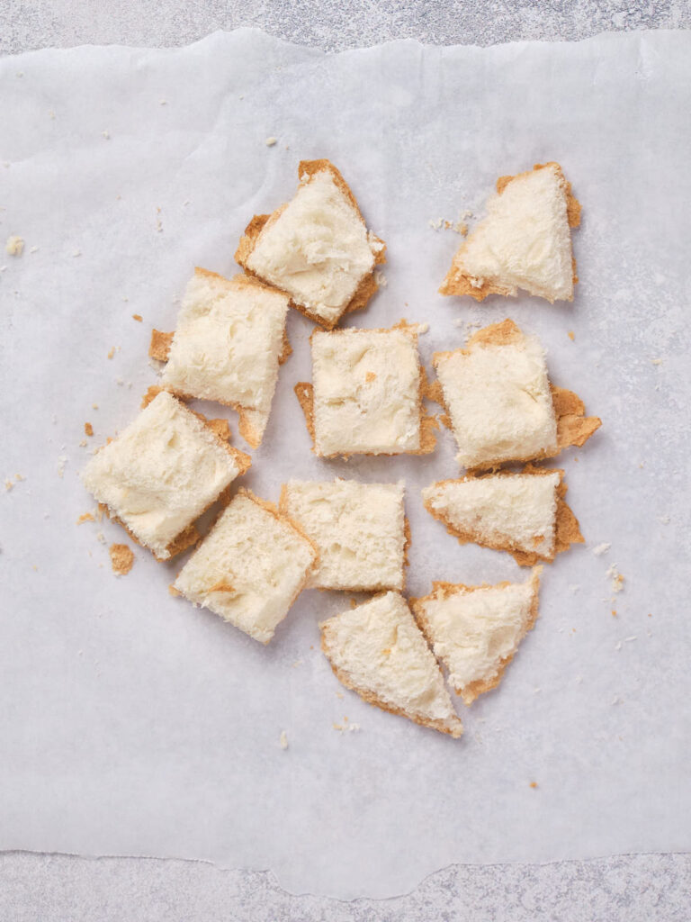 Crumbled shortbread cookies with cream topping scattered on parchment paper.