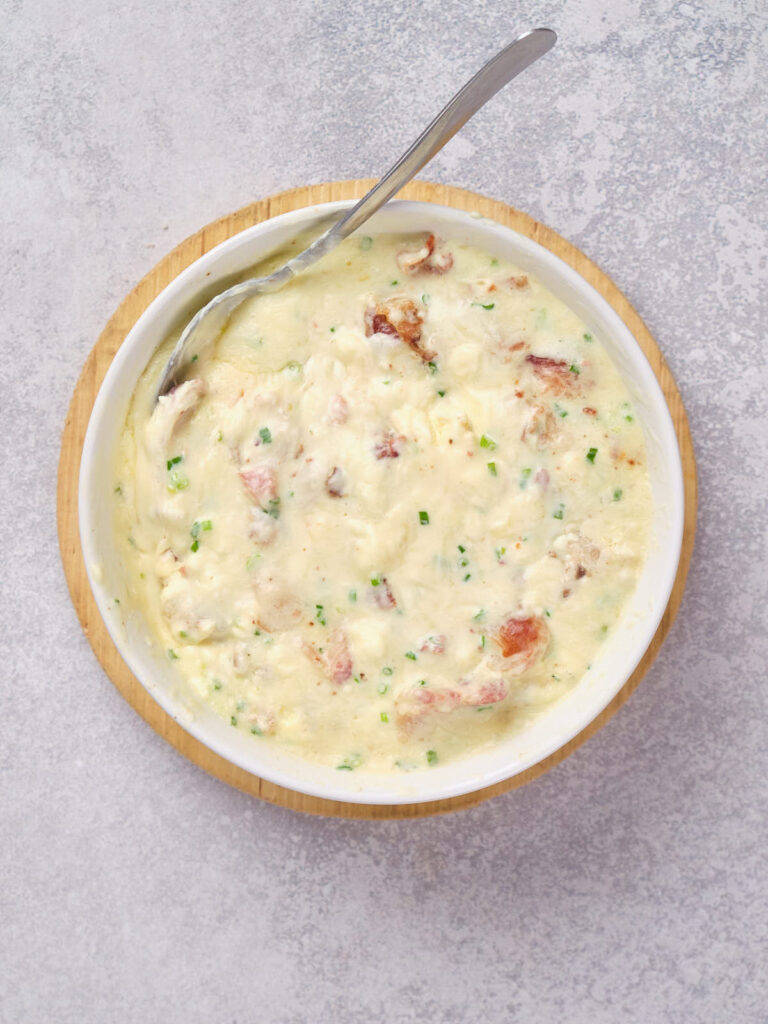 A bowl of creamy clam chowder with visible chunks of clams and sprinkled with chopped chives.