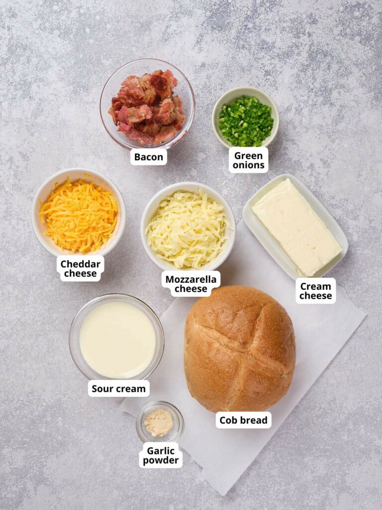 Ingredients for cheese and bacon cob loaf each in separate bowls on a gray surface.