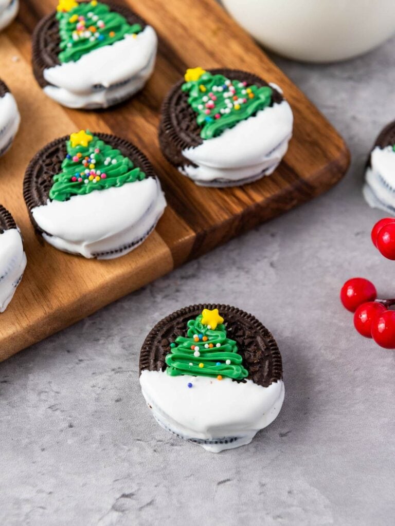 Chocolate cookies half-dipped in white icing, decorated with green icing Christmas trees and sprinkles.