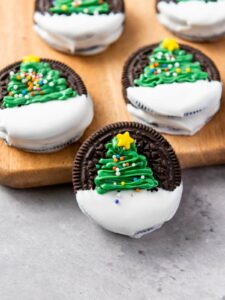 Chocolate sandwich cookies partially dipped in white icing, decorated with green Christmas tree designs.