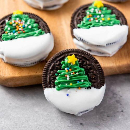 Chocolate sandwich cookies partially dipped in white icing, decorated with green Christmas tree designs.