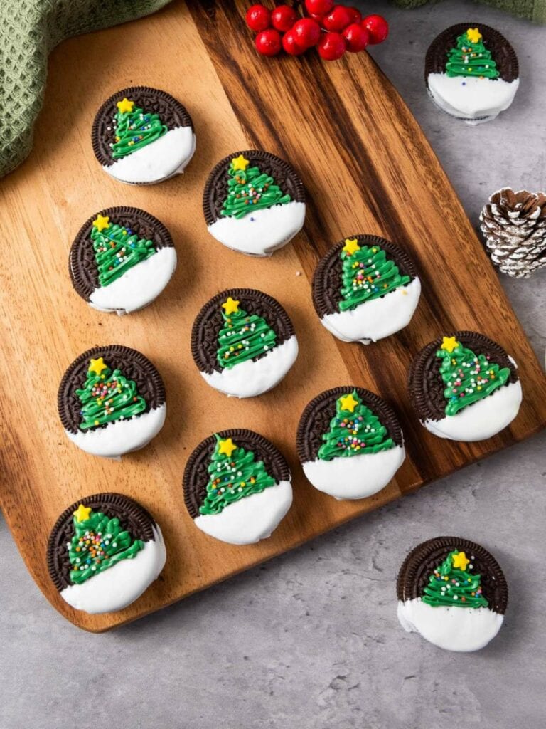 A wooden board with cookies decorated with green Christmas trees and white frosting.