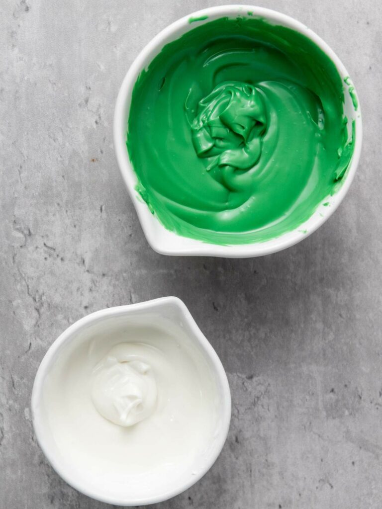 The top bowl contains green icing, and the bottom bowl contains white icing.