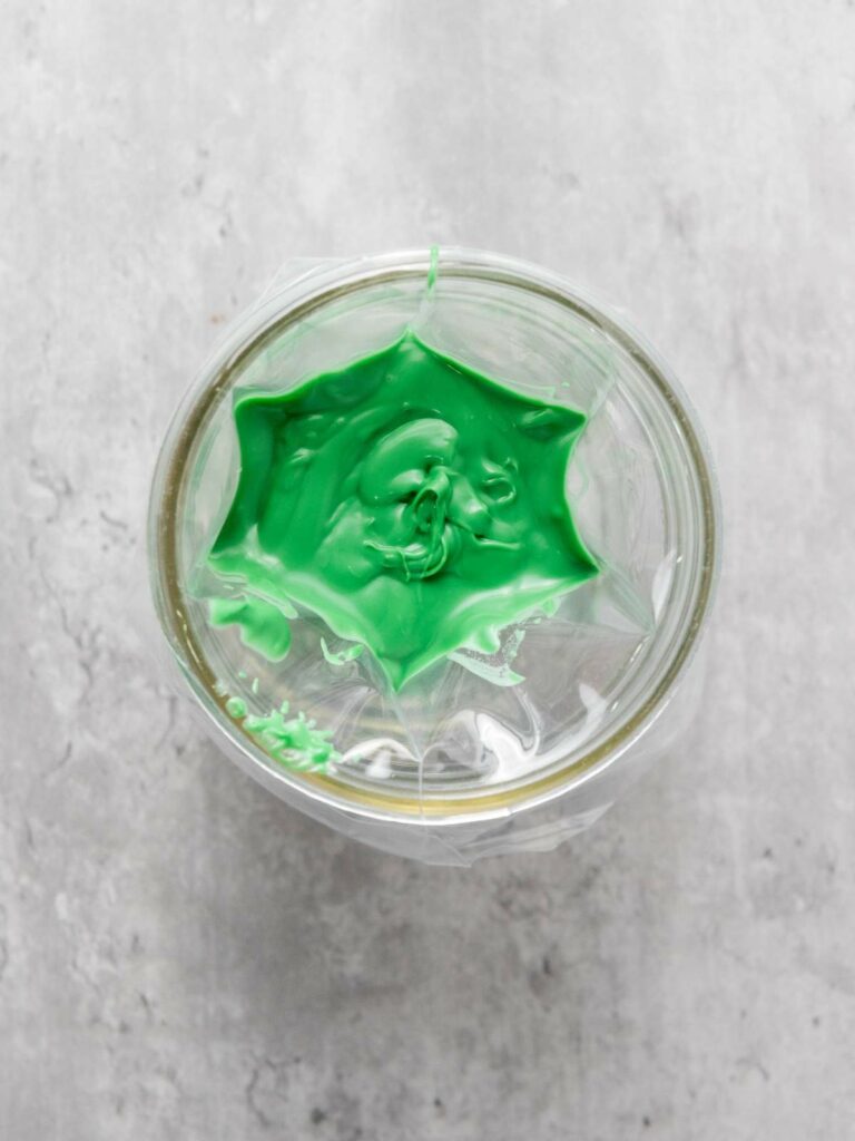 A glass jar filled with green paint, covered with plastic wrap.