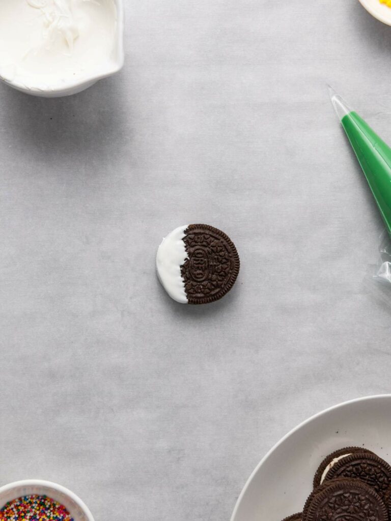 A chocolate sandwich cookie partially dipped in white icing on a gray surface.