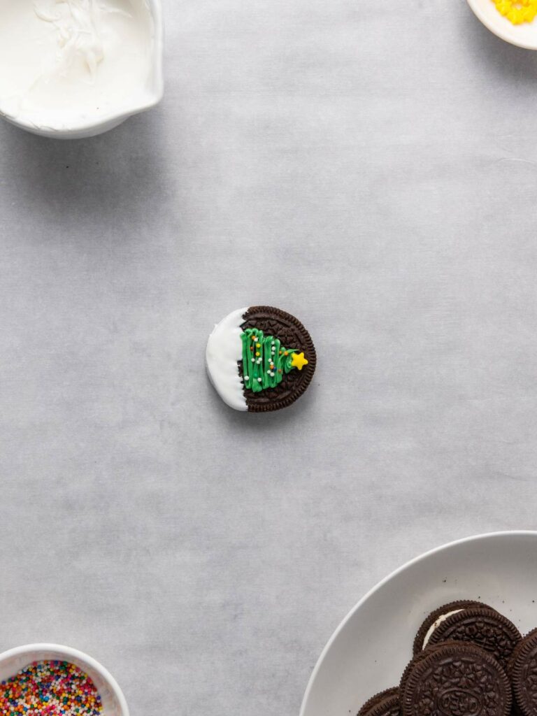 A chocolate sandwich cookie partially dipped in white icing, decorated with a green icing Christmas tree and a yellow star.