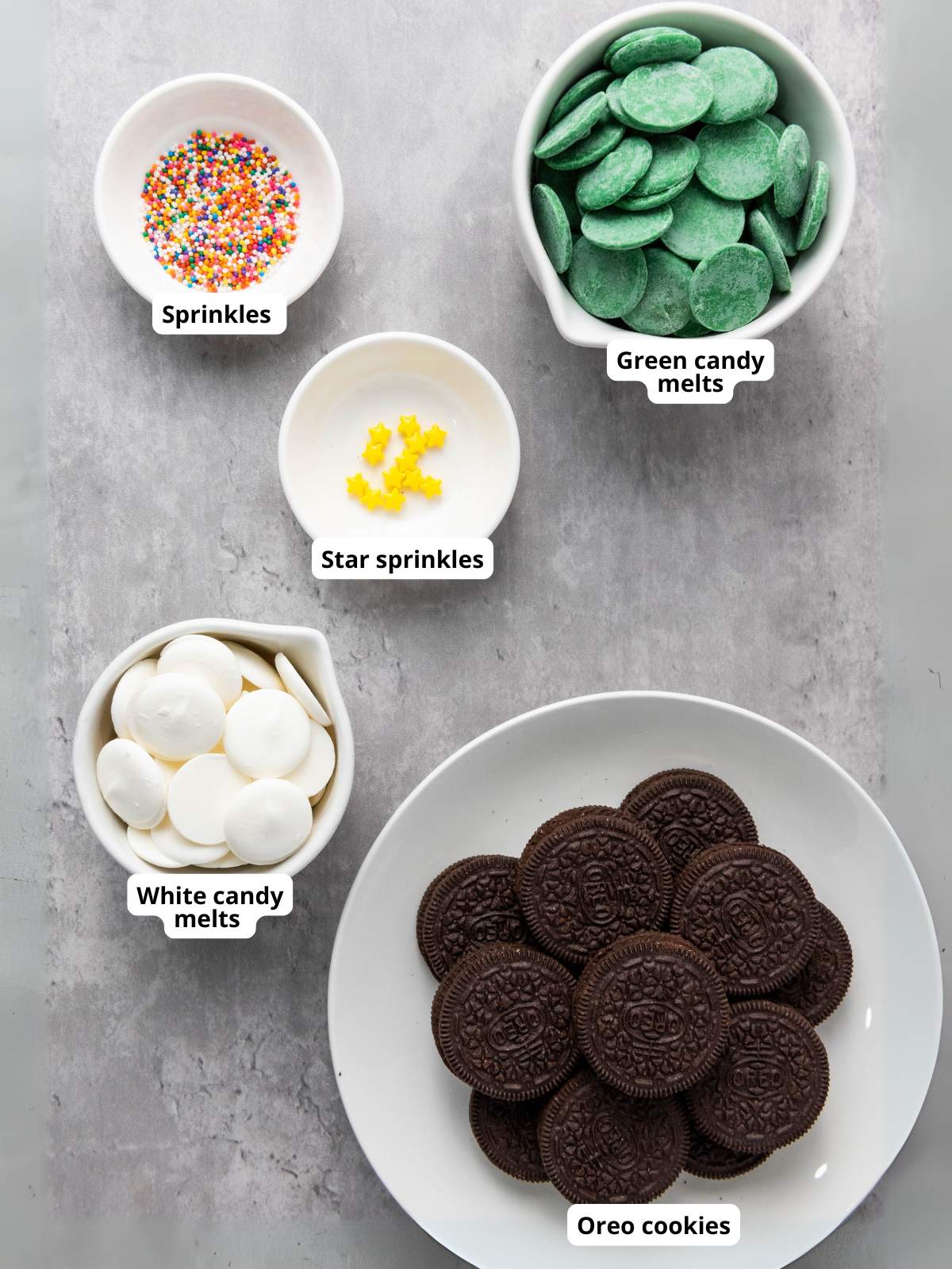 Various toppings and ingredients arranged on a table: sprinkles, star sprinkles, green and white candy melts, and Oreo cookies.