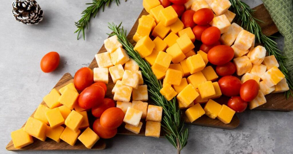 Cheese cubes and cherry tomatoes arranged on a wooden board in a Christmas tree shape, garnished with rosemary.