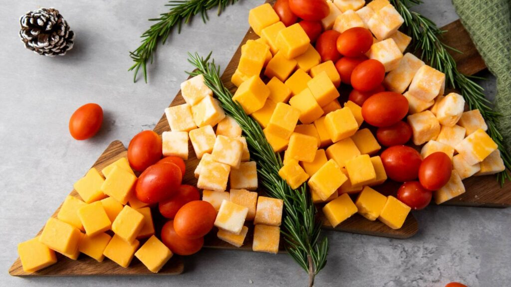 Cheese cubes and cherry tomatoes arranged on a triangular wooden board, garnished with rosemary sprigs.