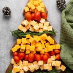 Food arranged on a tree-shaped board with cheese cubes, cherry tomatoes, and rosemary sprigs.