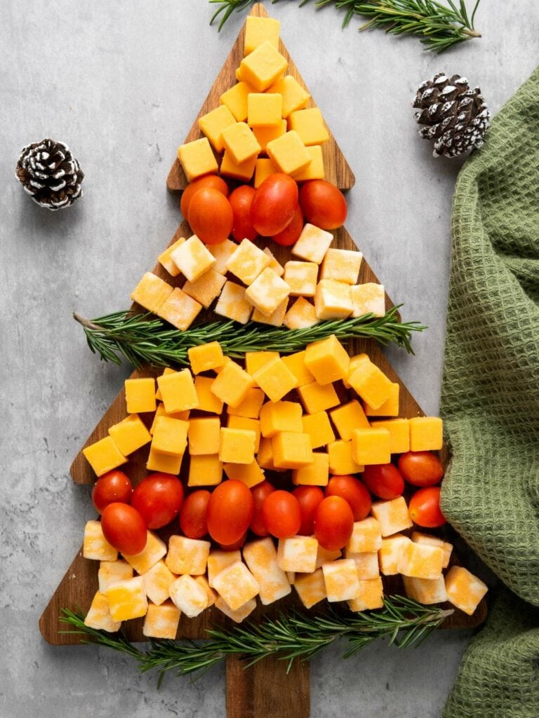 Food arranged on a tree-shaped board with cheese cubes, cherry tomatoes, and rosemary sprigs.